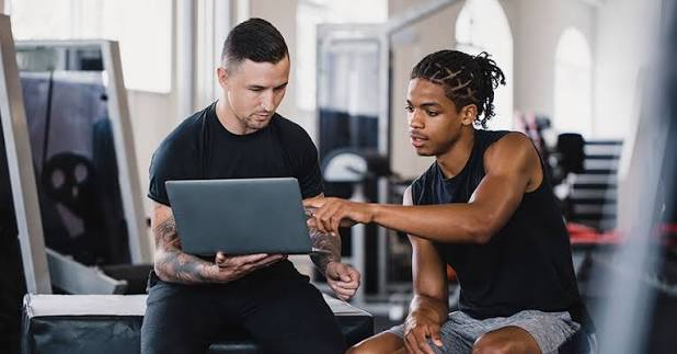 Coach and client reviewing progress together on a laptop in a gym