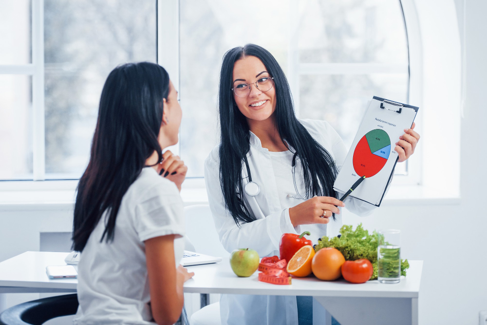 Health coach smiling while showing a nutrition chart to a client, with fresh fruit and vegetables on the desk